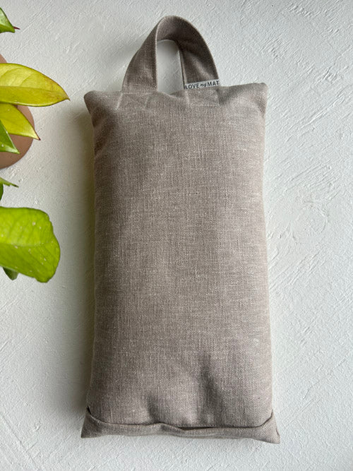 taupe sandbag laying flat on white background with a plant next to it