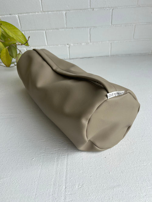 Side view of a brown vinyl yoga bolster on a white surface and against a white background