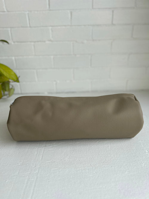 Taupe Brown Coloured Vinyl mini round bolster on a white surface and against a white brick background