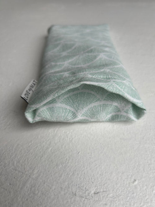 Light green fabric  eye pillow with a subtle pattern on a white surface