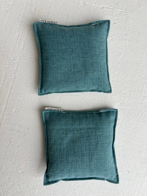 Two knee pillows for yoga in a teal fabric placed on a white surface.