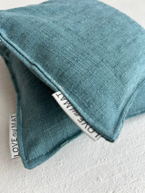 Close up of teal fabric yoga knee cushions on a white surface.