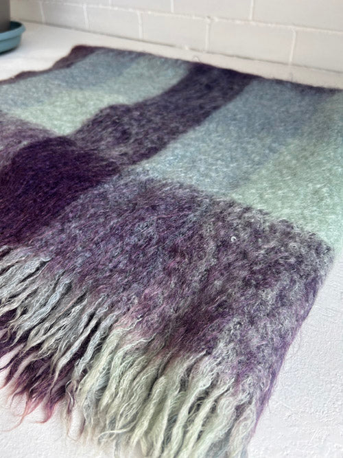 Multicolored woven throw blanket with fringe on a white floor.