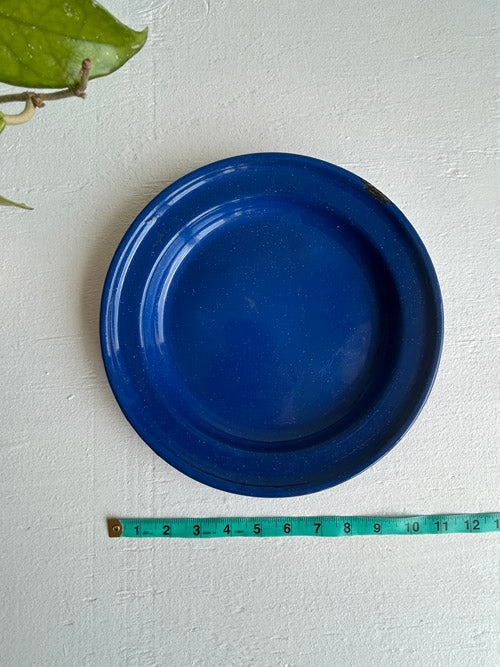Blue enamel plate on a white surface with a measuring tape for scale.