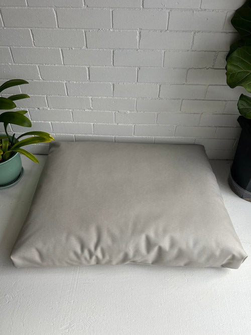 Beige meditation floor cushion on a white surface with a white brick wall background