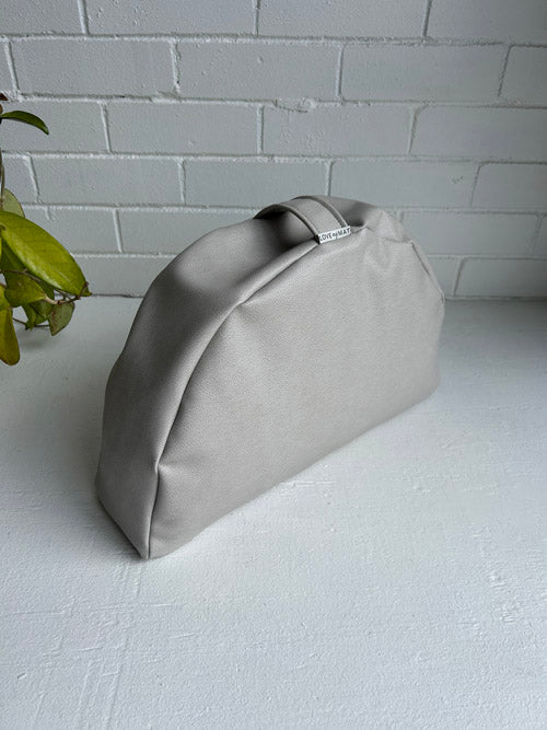 Light warm Grey handbag on a white surface with a light grey brick wall background