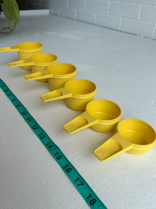 Set of yellow measuring cups on a white surface with a tape measure for scale.
