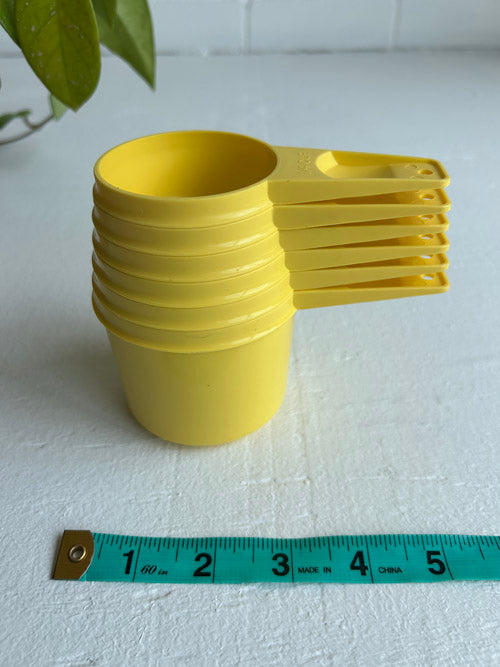 Stack of yellow plastic cups with a measuring tape for scale on a white surface.