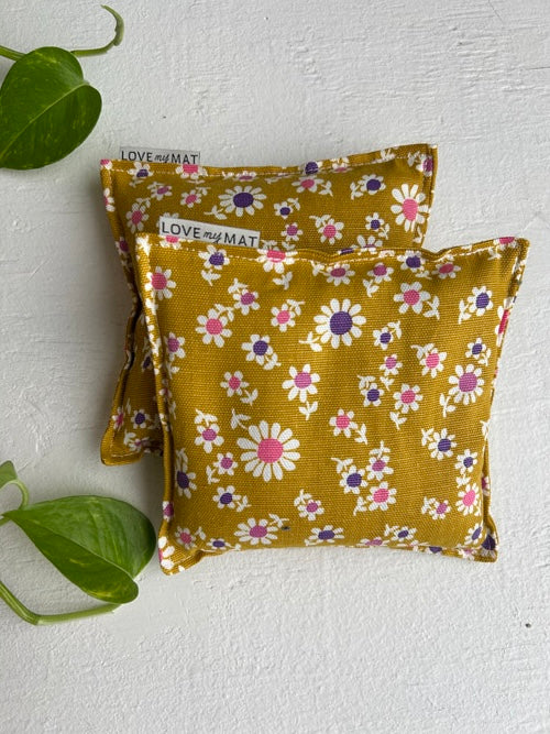 Two mustard yellow fabric knee pillows with floral patterns on a white background.